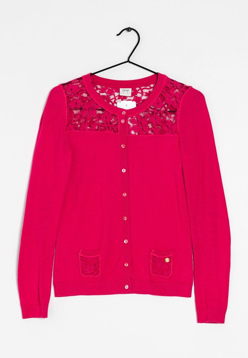 Cardigan rose vif boutonné avec un empiècement en dentelle et de petites poches devant, suspendu à un cintre noir sur un fond blanc.