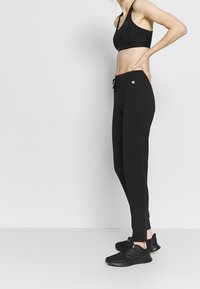 Schwarzes Sportoutfit bestehend aus einem enganliegenden Sport-BH und schmal zulaufenden Jogginghosen, gestaltet mit einem Kordelzug an der Taille und Logo-Akzenten.