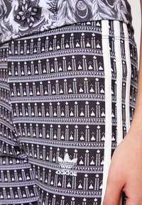 Svart och vit mönstrade leggings med vertikala vita ränder, tillverkade av mjukt tyg. Har en Adidas-logotyp i vitt nära sömmen på sidan.