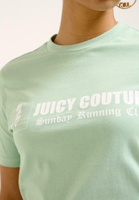 Šviesiai žalia medvilninė marškinėliai su balta užrašu: "JUICY COUTURE Sekmadienio Bėgimo Klubas" ir grafika su bėgiku kairėje pusėje. Trumpomis rankovėmis.