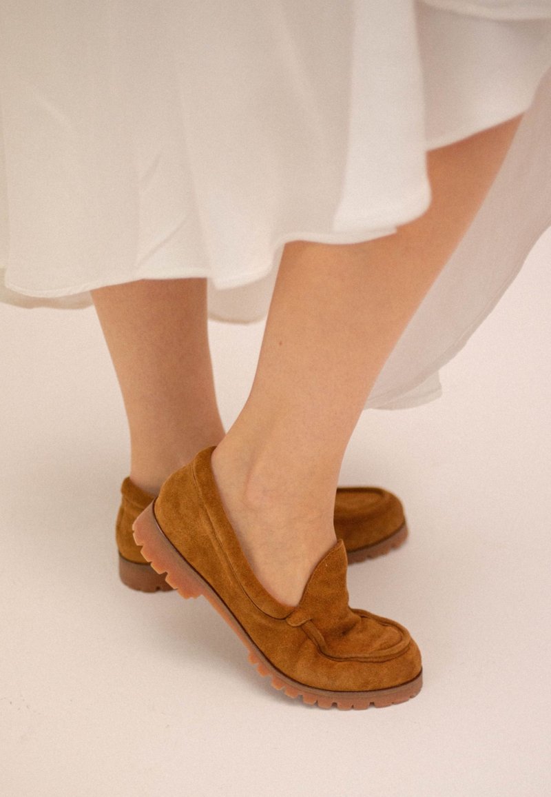 Brązowe zamszowe mokasyny z wyściełanym noskiem i grubą gumową podeszwą, o teksturowanym wykończeniu i zaokrąglonym kształcie.