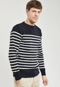 Maglione a righe blu navy e bianco, con maniche lunghe, collo rotondo e bottoni decorativi sulla spalla. Tessuto lavorato a maglia con polsini a costine.