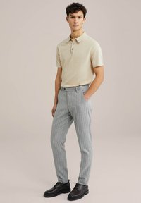 Beige polo krekls ar īsajiem piedurknēm, kopā ar gaiši pelēkiem raibajiem biksēm. Melni apavi noslēdz tēlu.