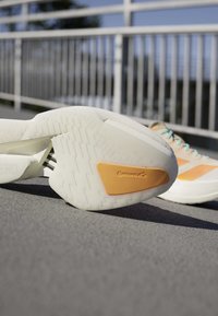 Witte en beige hardloopschoenen op asfalt met focus op de zool met een gele Continental-logo gripsectie.