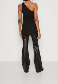 Top negro de un solo hombro con diseño fruncido, hecho de tejido texturizado con un brillo sutil, combinado con pantalones de cuero negro de tiro alto.