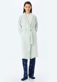Bata de baño de felpa verde claro con cintur�ón atado, combinada con pantalones azul marino con un patrón de renos. Textura suave, diseño hasta las rodillas.