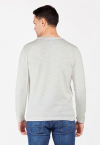 Maglietta a maniche lunghe grigia chiara con scollo rotondo, texture liscia e tessuto leggermente strutturato. Abbinata a jeans blu medio.