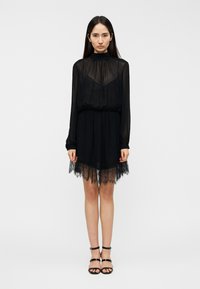 Μαύρο φόρεμα με διαφανείς μακριές μανίκες, σούρες στη μέση και δαντέλα στο τελείωμα. Λείο ύφασμα, μήκος μέχρι το γόνατο. Μαύρα σανδάλια με λουράκια.