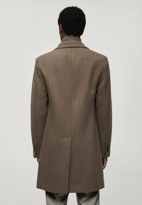Bruine wollen jas met een gestructureerde silhoutte, met een notch-kraag en een split aan de achterkant. Voorzien van knopenmanchetten en een minimalistisch ontwerp.