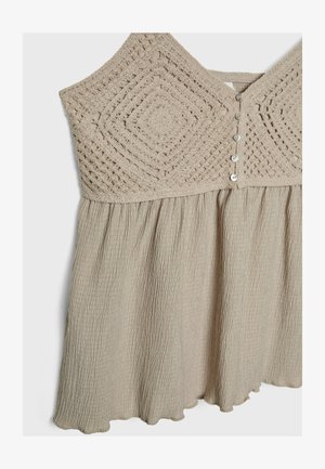 Light beige dress featuring a textured crochet bodice and a gathered skirt. Insets have button closures and a wavy hemline. Soft, flowy fabric.