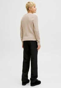 Jasnobrązowy sweter w prążki z długim rękawem, w połączeniu z czarnymi luźnymi spodniami i czarnymi butami. Prosty design i neutralne kolory.