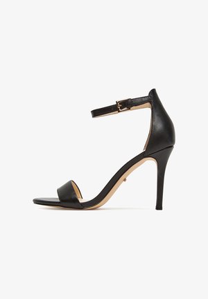 Czarna sandałka na wysokim obcasie z cienkim paskiem wokół kostki, otwartym noskiem i błyszczącym wykończeniem ze skóry; ozdobiona złotą klamrą.