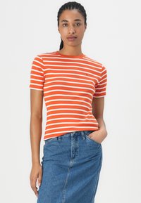 Stripet kortermet t-skjorte i lys orange og hvit, med rund hals og en liten logo på brystet, sammen med et denimskjørt.
