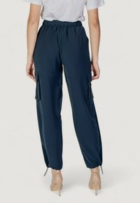 Pantaloni cargo blu navy con vita arricciata, polsini elastici e due tasche laterali. Il tessuto sembra morbido con una superficie liscia.
