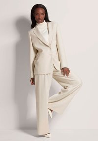 Crème-kleurig op maat gemaakt kostuum met wijde broekspijpen en een enkelknopen blazer. Glad textuur, met een subtiel streepjespatroon.