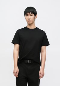 Čierne bavlnené tričko s okrúhlym výstrihom, krátkymi rukávmi a voľným strihom, skombinované s čiernymi nohavicami a čiernym opaskom.