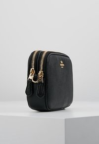 Musta tekstuurinen nahkalaukku, jossa on kaksi kultasävyistä vetoketjua, suorakulmainen muoto ja hienovarainen brändilogo edessä. Kompakti ja kestävä muotoilu.