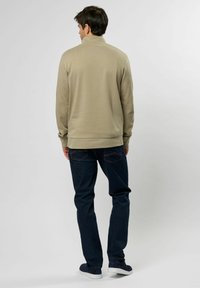 Beige genser med høy krage, ribbestrikkede mansjetter og nederkant, sammen med mørkeblå jeans. Glatt tekstur, avslappet design.
