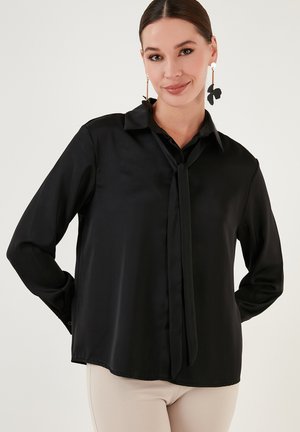 Black satin blouse with a tie at the collar, long sleeves, and a relaxed fit. Smooth texture with a polished sheen.