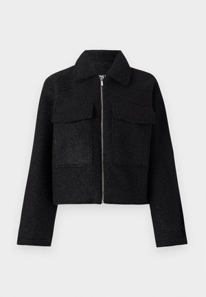 Chaqueta corta negra hecha de tela texturizada, con cierre de cremallera, cuello y dos bolsillos frontales. Diseño sencillo sin patrones.