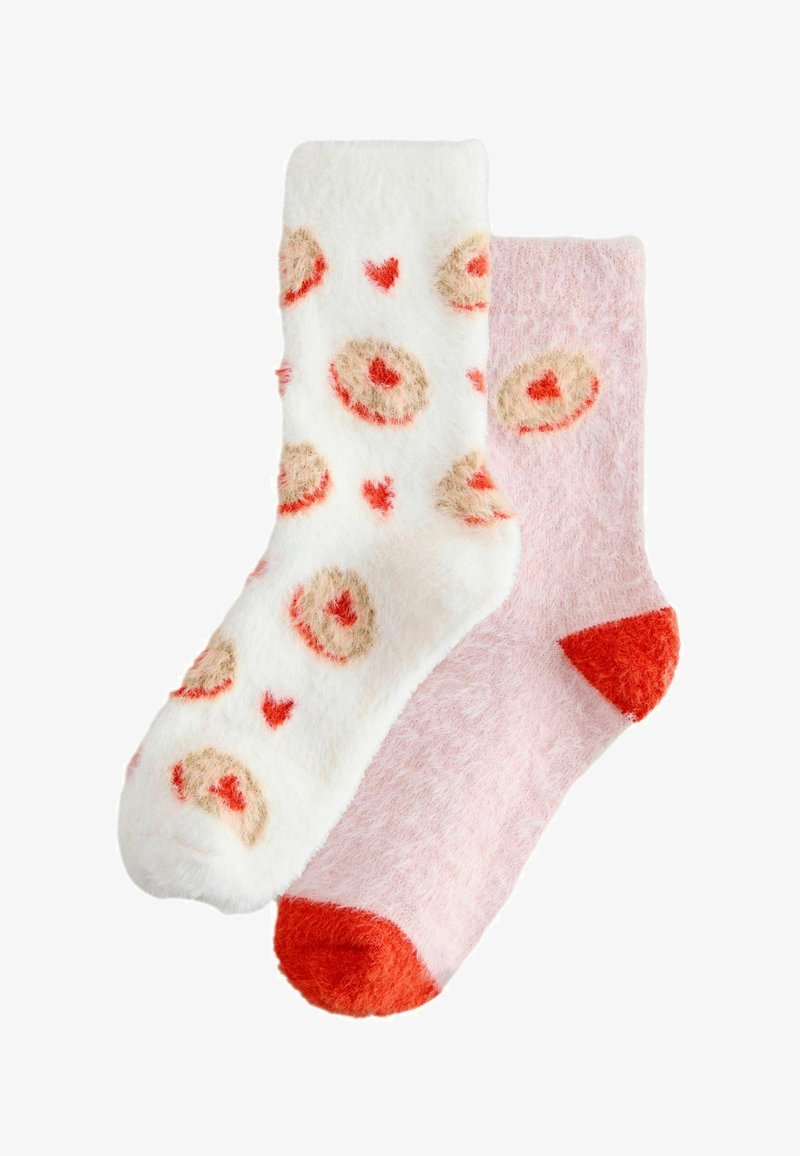Paire de chaussettes duveteuses, l'une blanche avec des motifs de cœurs et de cercles rouges et beiges, l'autre rose clair avec des accents rouges au talon et aux orteils.