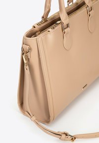 Beige leren handtas met gouden hardware, dubbele handvatten aan de bovenkant en een afneembare schouderriem. Beschikt over ritscompartimenten en heeft een gestructureerde vorm.