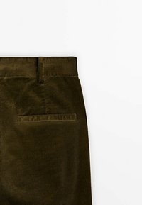 Pantalon en velours côtelé vert foncé avec une poche passepoilée à l'arrière et une boucle de ceinture, présenté sur fond blanc.