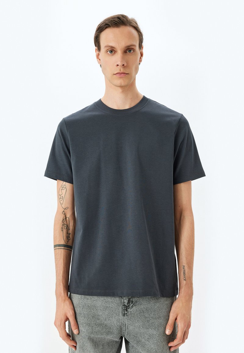 Camiseta de manga corta gris oscuro con cuello redondo, hecha de una tela suave. Presenta un dobladillo recto y detalles de costura sutiles.