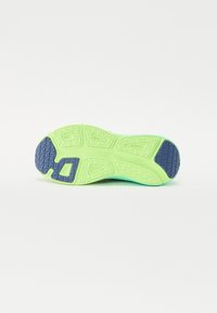 Sneaker såle med en lys grønn gummi base med teksturerte gripe mønstre og en mørk blå akcent på hælen.