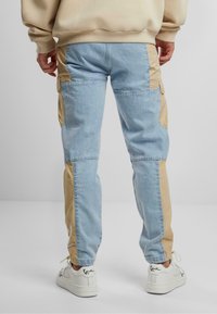 Helle blaue Denim-Cargo-Hosen mit beigefarbenen Seitenteilen und Bündchen. Sie verfügen über Taschen und einen lässigen Schnitt, kombiniert mit weißen Sneakers.