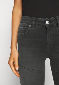 Jeans de denim negro con un diseño ajustado, que cuentan con bolsillos frontales y un cierre de botón plateado. Textura suave con un ligero desvanecimiento.
