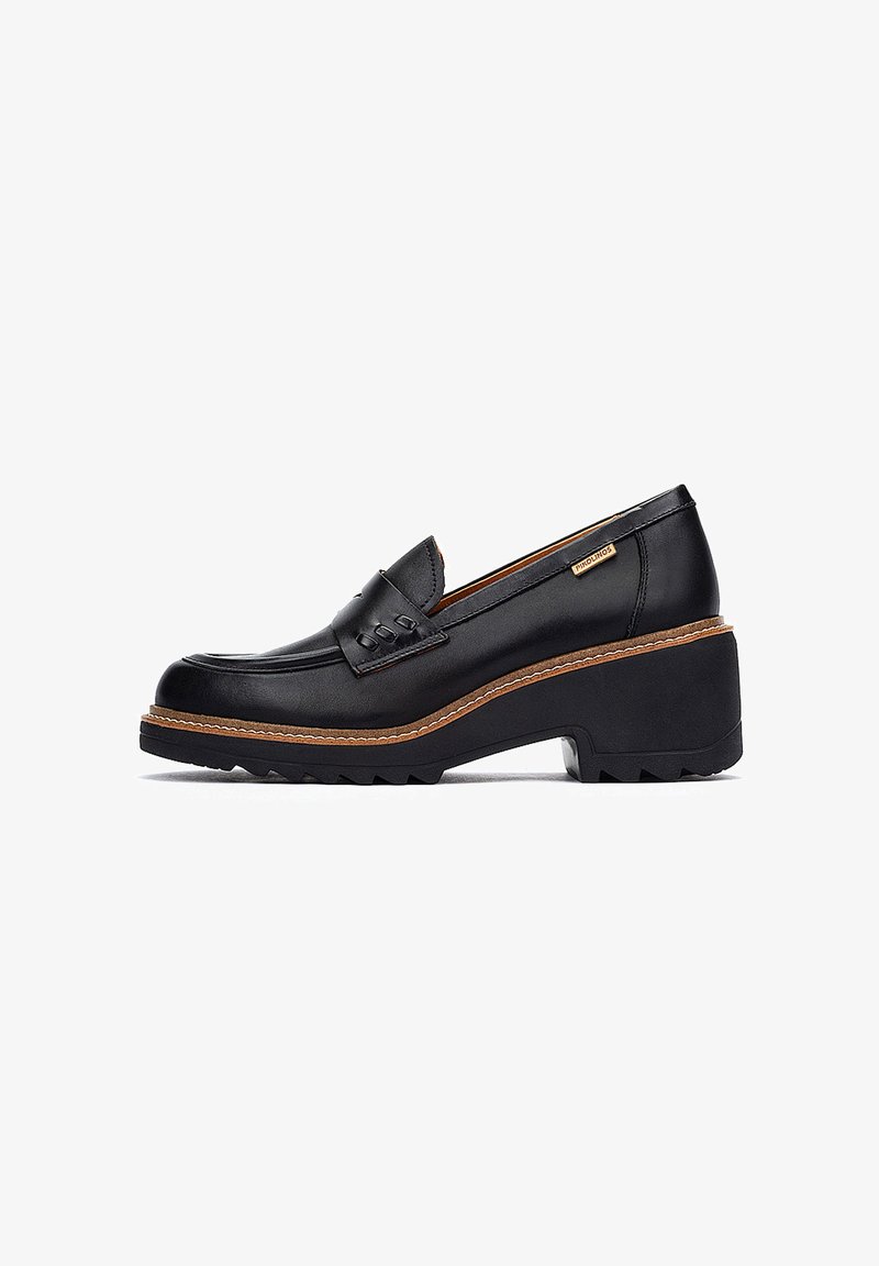 Mocasín de cuero negro con parte superior texturizada, punta redondeada y plataforma gruesa. Presenta una suela con zigzag y costuras decorativas en la pala.