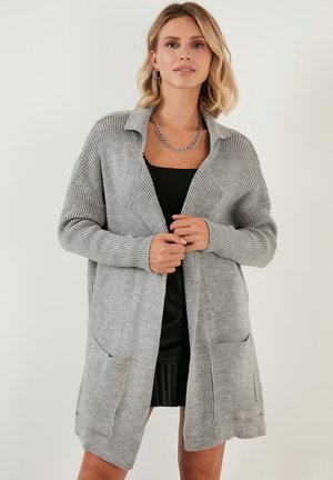 Grijze gebreide cardigan met kraag, open voorkant en twee voorkruiszakken. Kenmerkt zich door verticale ribbels en een relaxte pasvorm. Soepele textuur.