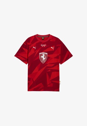 Czerwona bawełniana koszulka z geometrycznym wzorem, okrągłym dekoltem, krótkimi rękawami oraz centralnym białym logo Ferrari w kształcie tarczy.