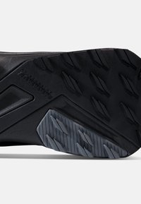 Semelle de chaussure en caoutchouc noir avec une surface texturée et un motif de bande de roulement multidirectionnel pour une meilleure adhérence. Comprend une semelle intermédiaire grise avec des accents géométriques.