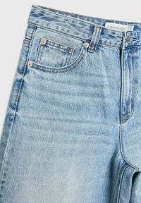 Jean en denim bleu clair taille haute avec poches avant, fermeture par boutons et étiquette de taille sur la ceinture indiquant la marque Stradivarius.