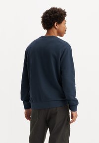 Donkerblauwe sweatshirt van zacht materiaal, met lange mouwen en een ronde hals. De achterkant heeft een gladde textuur en elastische manchetten.