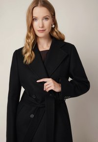Czarny płaszcz dwurzędowy z paskiem, z dużymi guzikami i kołnierzem z wyłogami. Gładka tekstura i dopasowany krój.