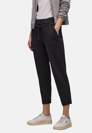 Sorte beskårne joggingbukser med elastisk linning, snøre og sidelommer, stylet med hvide sneakers og en lysegrå lynlåstrøje.