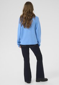 Lys blå tekstureret sweater med en løs pasform, parret med mørke flare jeans og sorte platform støvler, set fra ryggen.