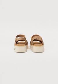 Tan suede sandals with open heel and multiple straps, featuring a thick white sole for added height and stability.