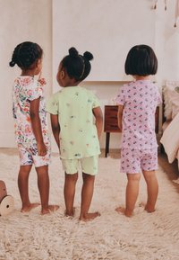 Tres niños llevan pijamas de manga corta: de estampado floral (blanco), verde pastel liso y lavanda estampada. Tejido de algodón suave, corte casual.