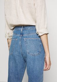 Vaaleansiniset farkut, joissa on korkea vyötärö, kahdella takataskulla ja rennolla leikkauksella. Kankaan pinta on pehmeä.