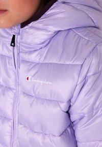 Giacca imbottita lavanda con chiusura a zip, design trapuntato e logo Champion sul davanti. Il materiale ha una texture liscia e lucida.