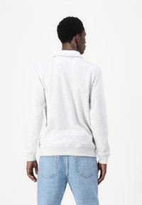 Lichtgrijze sweatshirt met een gebreide kraag, ribbels bij de mouwen en onderrand, en een gestructureerde stof. Gepaard met lichtgewassen denim jeans.