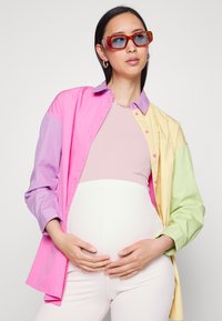Camisa em blocos de cor com painéis cor-de-rosa, lavanda, amarelo e verde; combinada com um top pastel justo e calças brancas com textura em rib. 