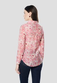 Ružová blúzka s paisley vzorom, dlhými rukávmi, golierom na gombíky a mierne zaobleným lemom. Vyrobená z ľahkej tkaniny.