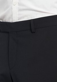 Črne hlače iz gladkega materiala z oprijetim krojem. Obesene na pasu z zanko za pas in sprednjim pregibom.