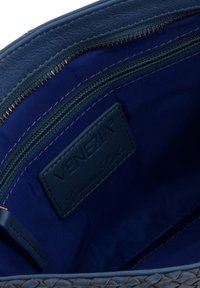 Wnętrze niebieskiej skórzanej torebki, z teksturowaną powierzchnią, kieszonką na zamek i metką z logo "VENEZIA" w dopasowanym odcieniu niebieskiego.