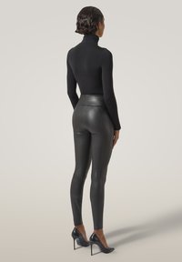 Svart polokrage topp i kombination med högmidjade, strukturerade svarta leggings och svarta högklackade skor, sedd bakifrån. Slät tygfinish.